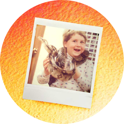 polaroid of a 7 year old girl with a blonde mullet and a HUGE grin, holding a python wrapped around her neck with on a gradient orange to yellow background